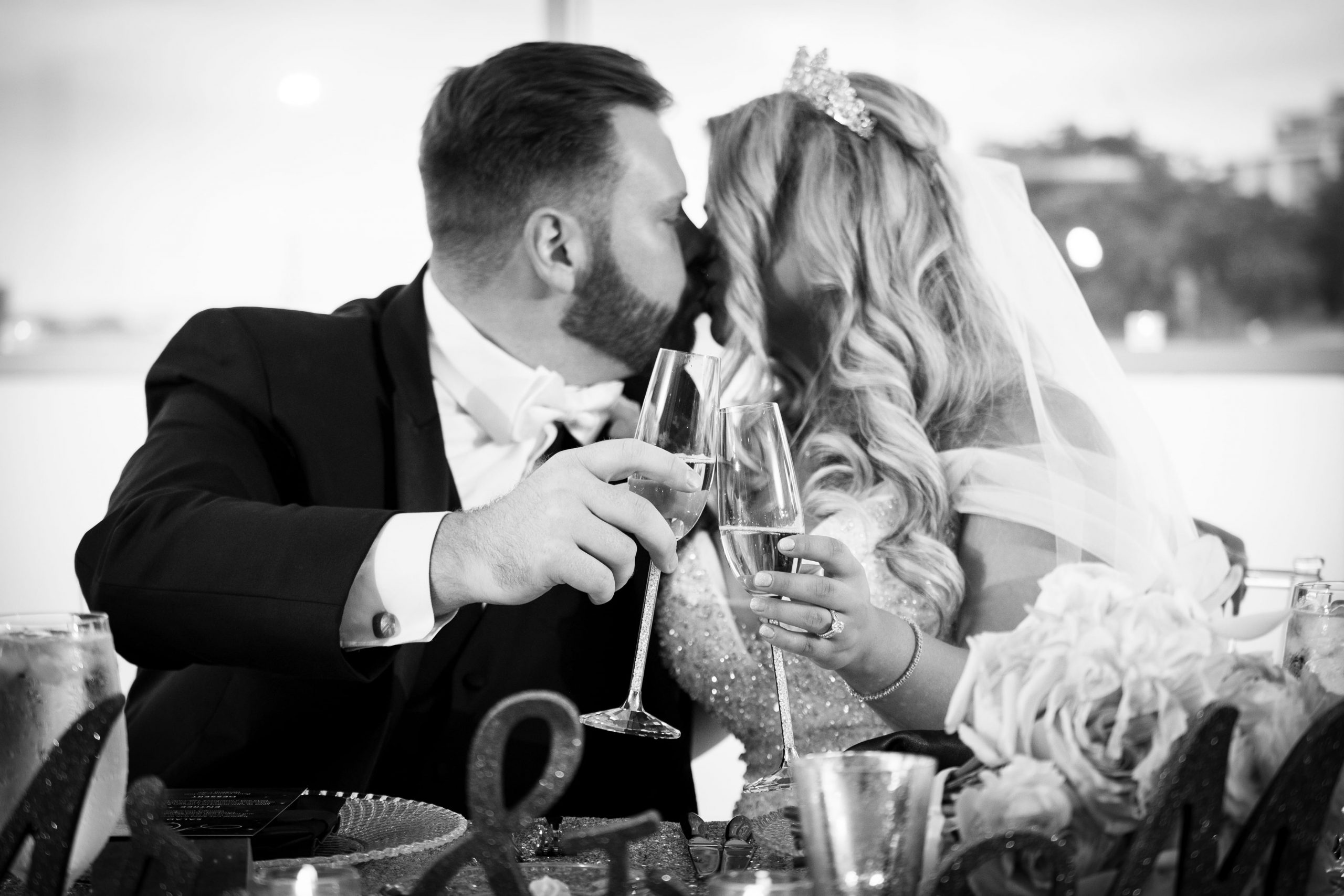 couple kissing and holding glasses at head table at reception