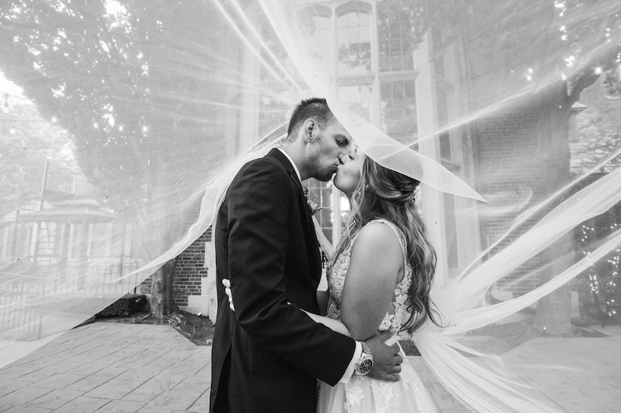 black and white of bride and groom kissing under wedding veil